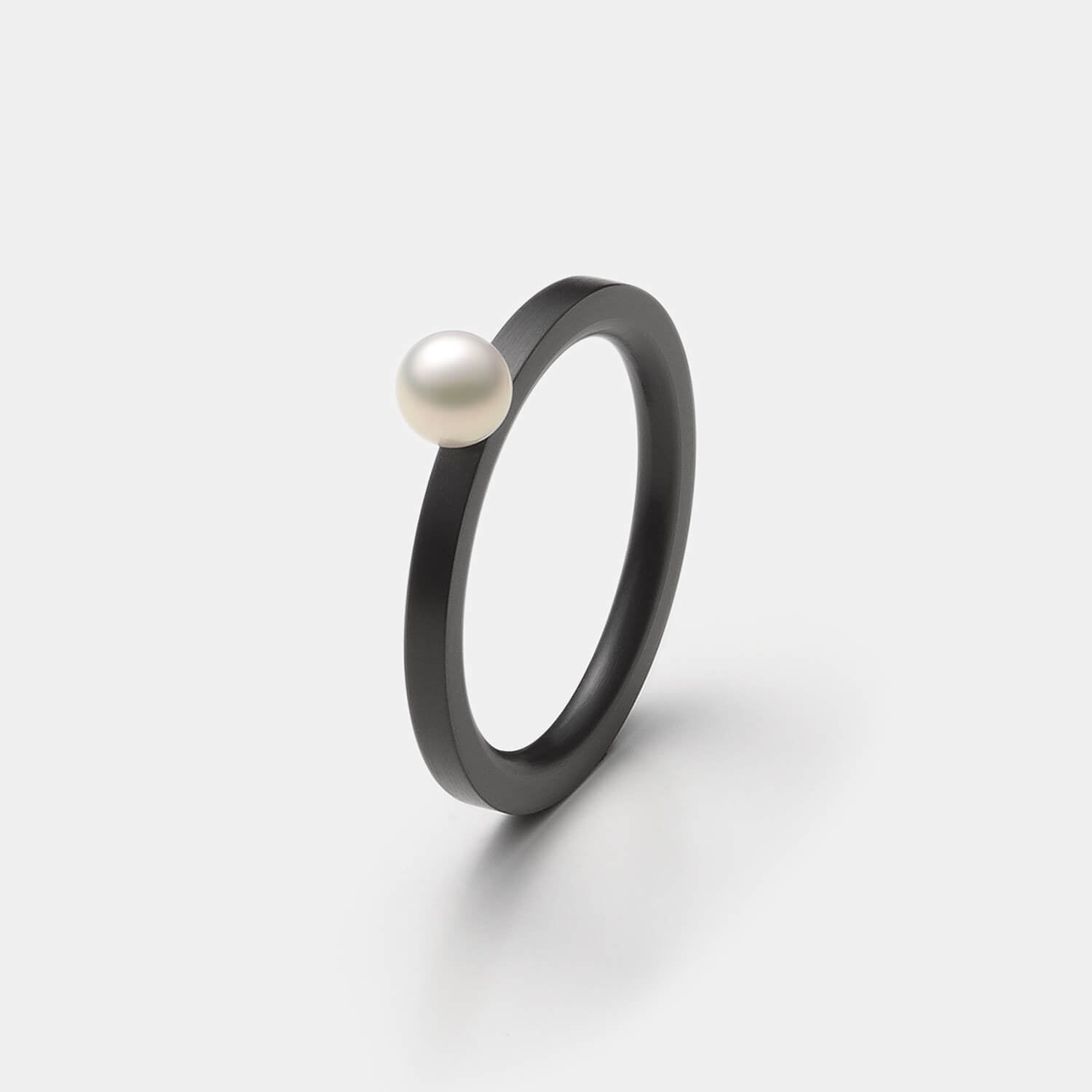 Gesamtansicht eines schmalen, schwarzen  Edelstahl-Rings mit echter, weißer Süßwasserperle von MONOMANIA.