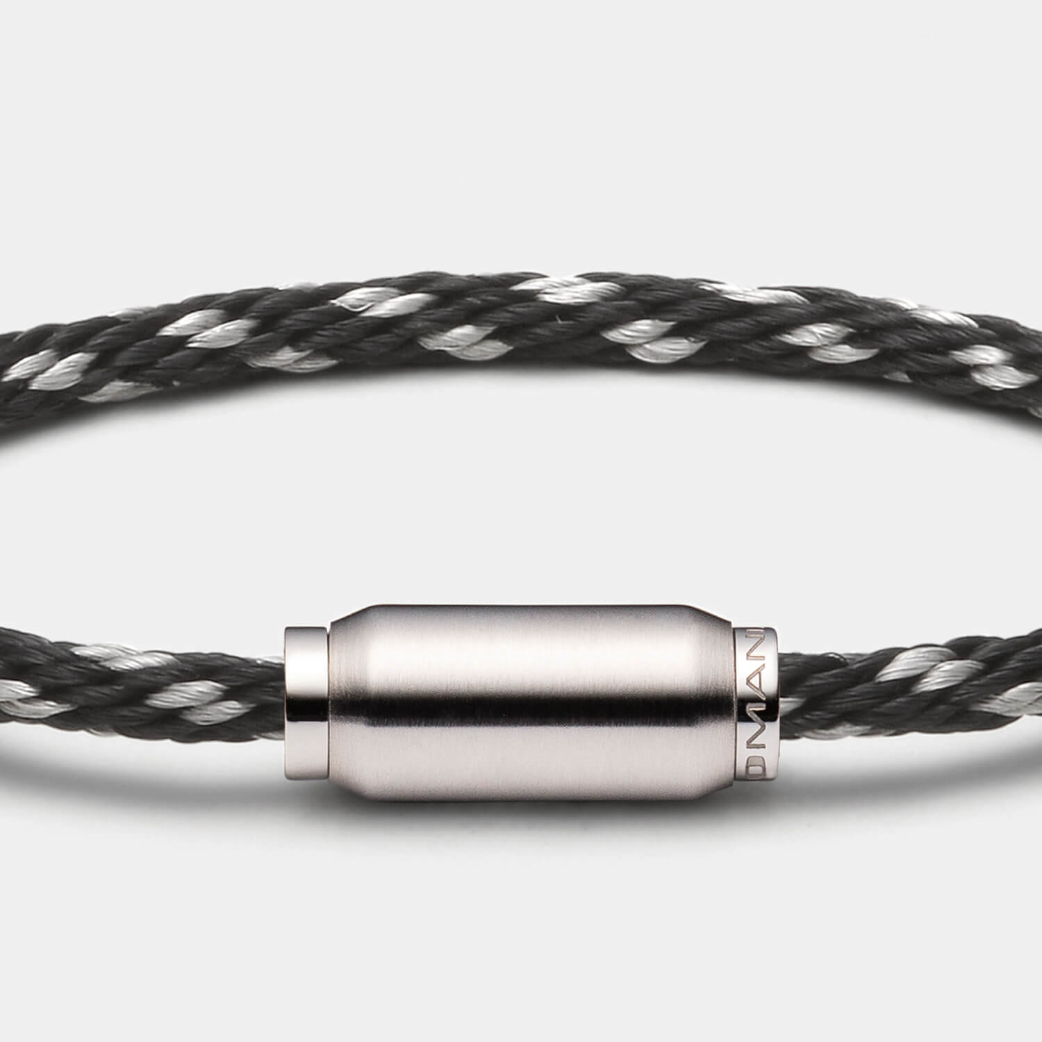 Gesamtansicht eines schicken Armbandes: Kombination aus gebürsteter, zylinderförmiger Hülse mit einem schwarzen Edelstahl-Materialmixband von MONOMANIA.