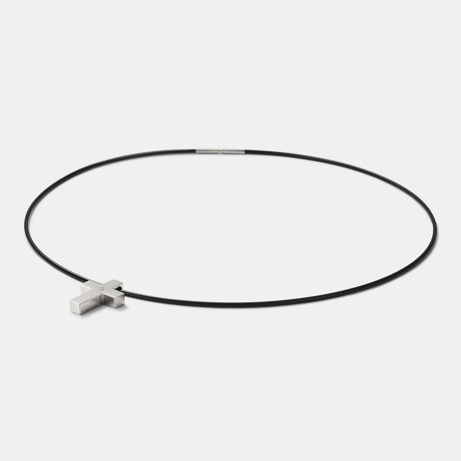 Perspektivische Detailansicht des kreuzförmigen Anhängers aus gebürstetem, antiallergenem Edelstahl mit einem gesetzten Diamanten an einem Kautschukband mit Bajonettverschluss von MONOMANIA.