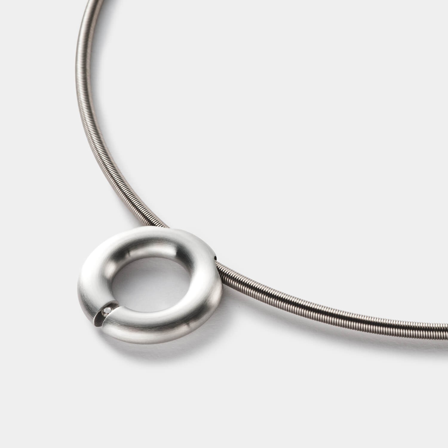 Detailansicht eines runden, gebürsteten Anhängers aus antiallergenem Edelstahl mit einem gesetzten Diamanten an einem Spiralcollier mit Bajonettverschluss von MONOMANIA.
