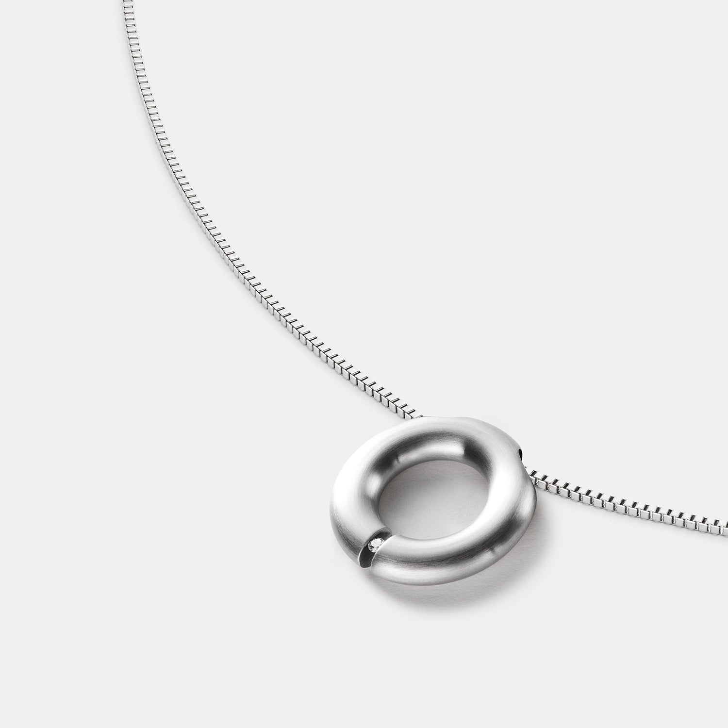 Detailansicht eines runden, gebürsteten Anhängers aus antiallergenem Edelstahl mit einem gesetzten Diamanten an einem Spiralcollier mit Bajonettverschluss von MONOMANIA.