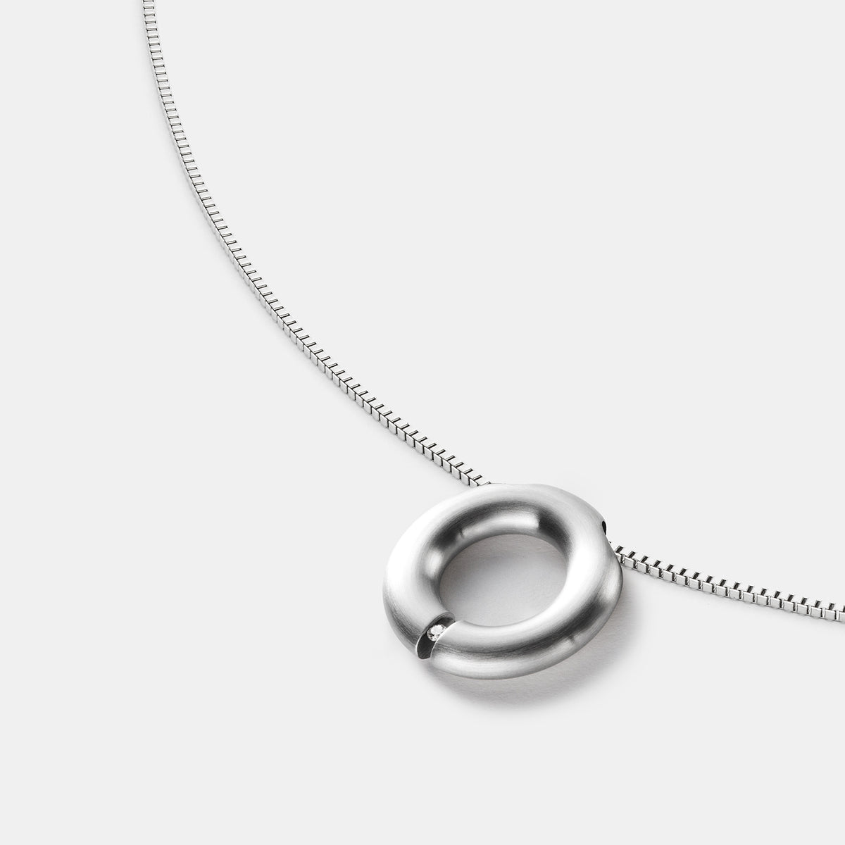 Detailansicht eines runden, gebürsteten Anhängers aus antiallergenem Edelstahl mit einem gesetzten Diamanten an einem Spiralcollier mit Bajonettverschluss von MONOMANIA.