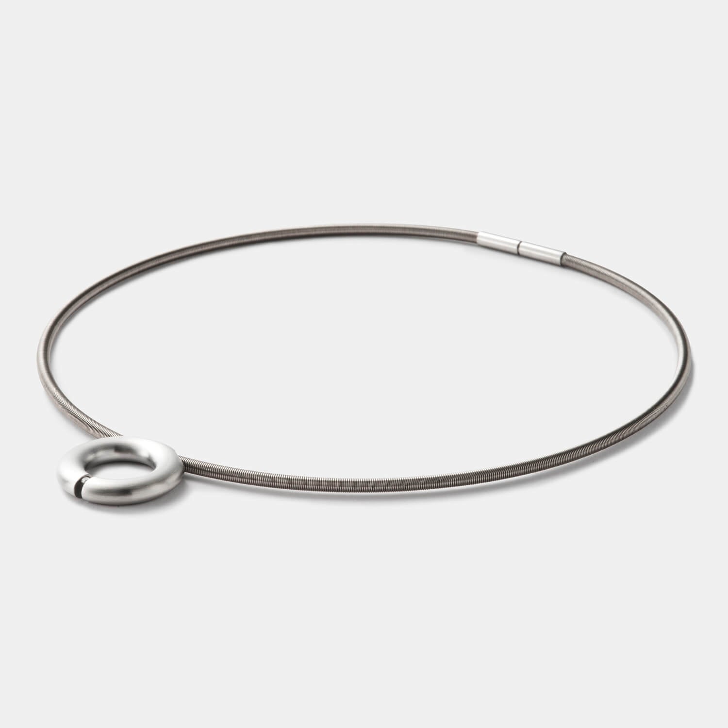 Detailansicht eines runden, gebürsteten Anhängers aus antiallergenem Edelstahl mit einem gesetzten Diamanten an einem Spiralcollier mit Bajonettverschluss von MONOMANIA.