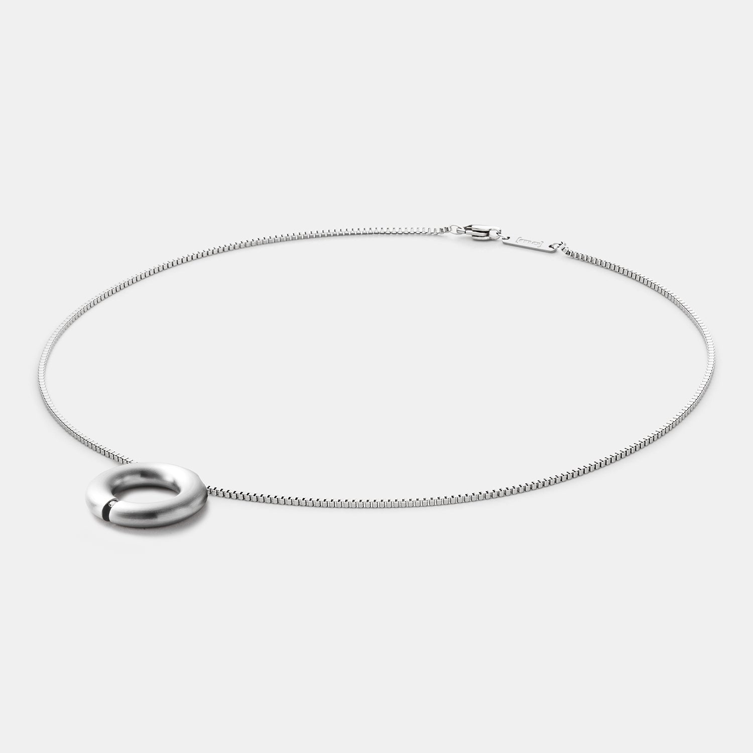 Detailansicht eines runden, gebürsteten Anhängers aus antiallergenem Edelstahl mit einem gesetzten Diamanten an einem Spiralcollier mit Bajonettverschluss von MONOMANIA.
