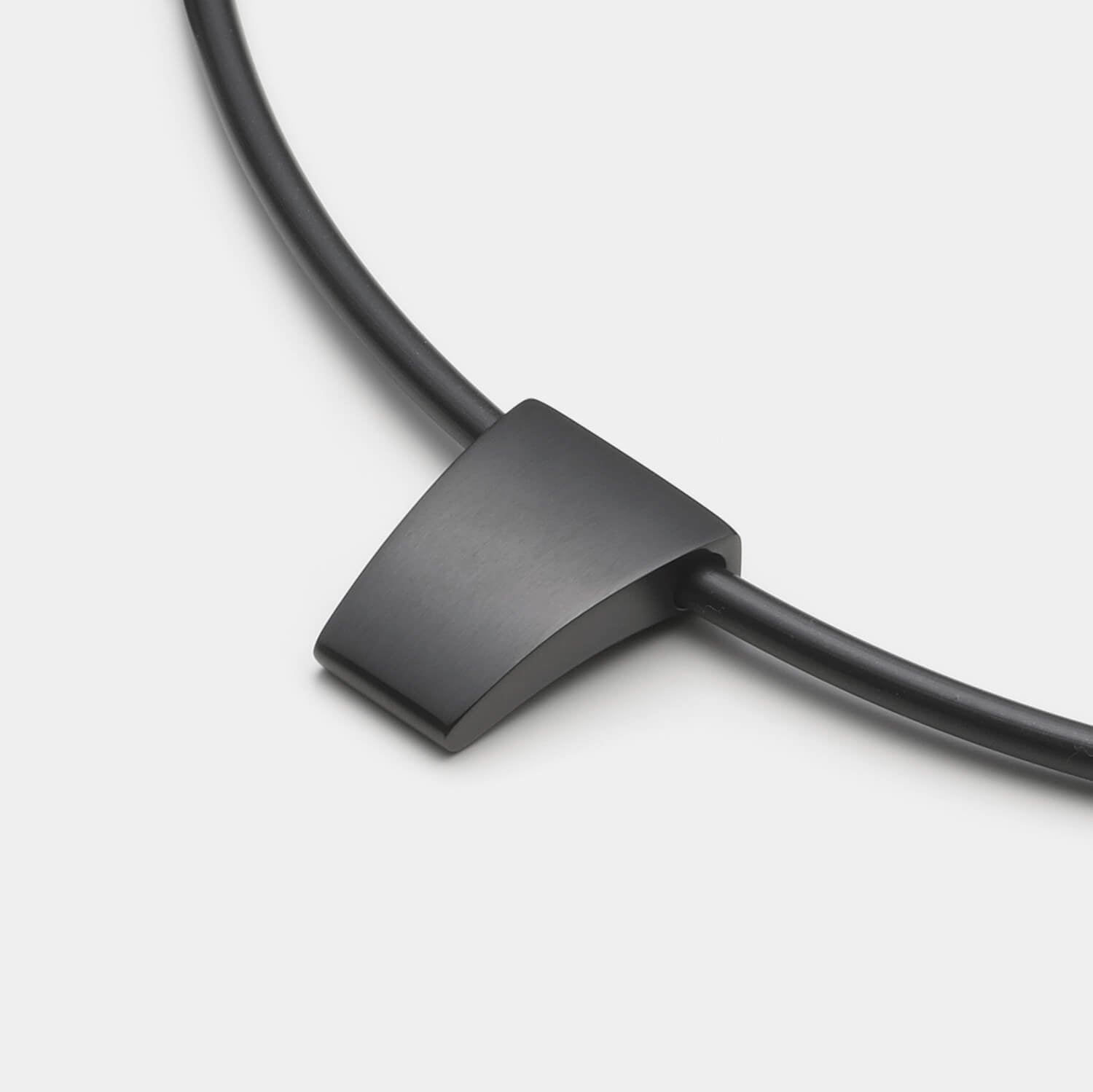 Detailansicht eines schlichten, schwarzen Anhängers aus antiallergenem Edelstahl an einem schwarzen Kautschukband von MONOMANIA.