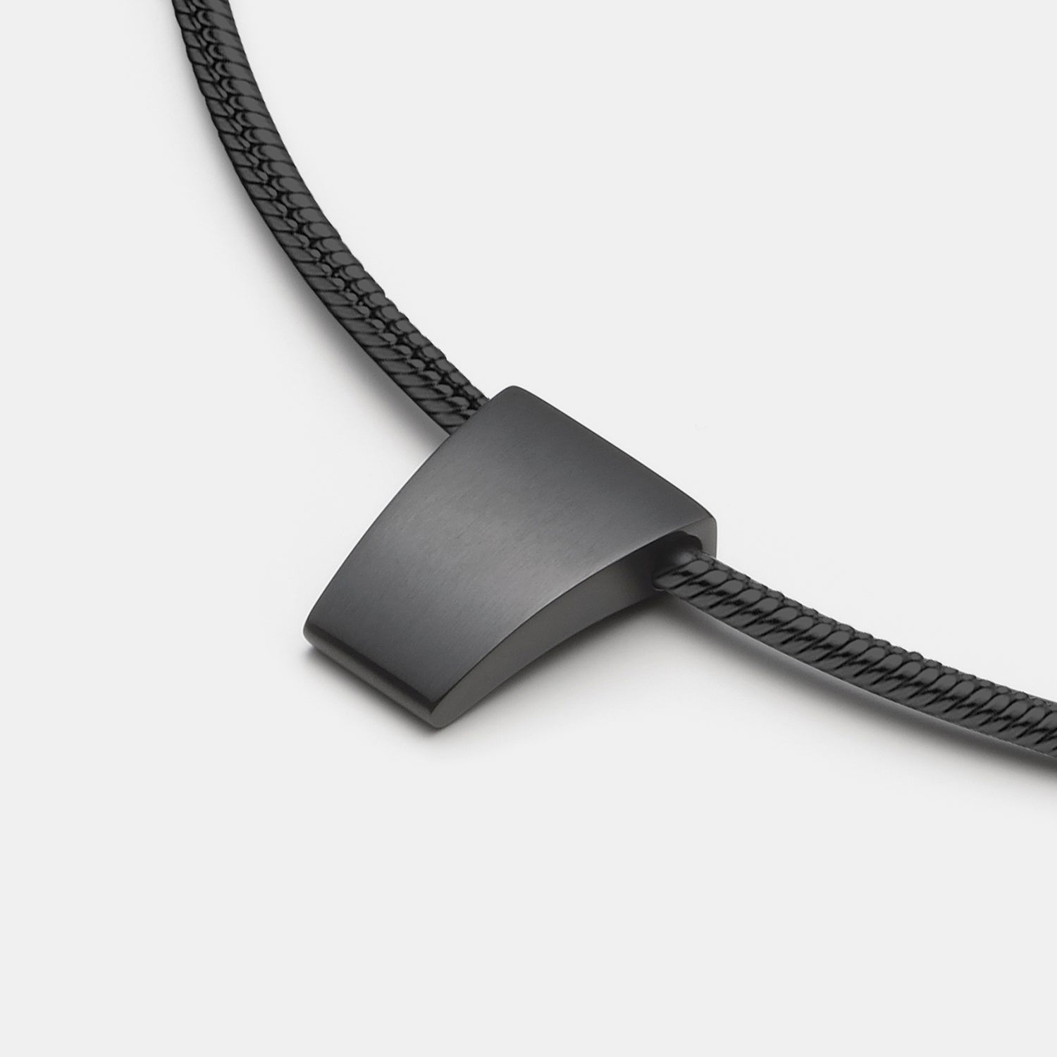 Detailansicht eines schlichten, schwarzen Anhängers aus antiallergenem Edelstahl an einem schwarzen Kautschukband von MONOMANIA.