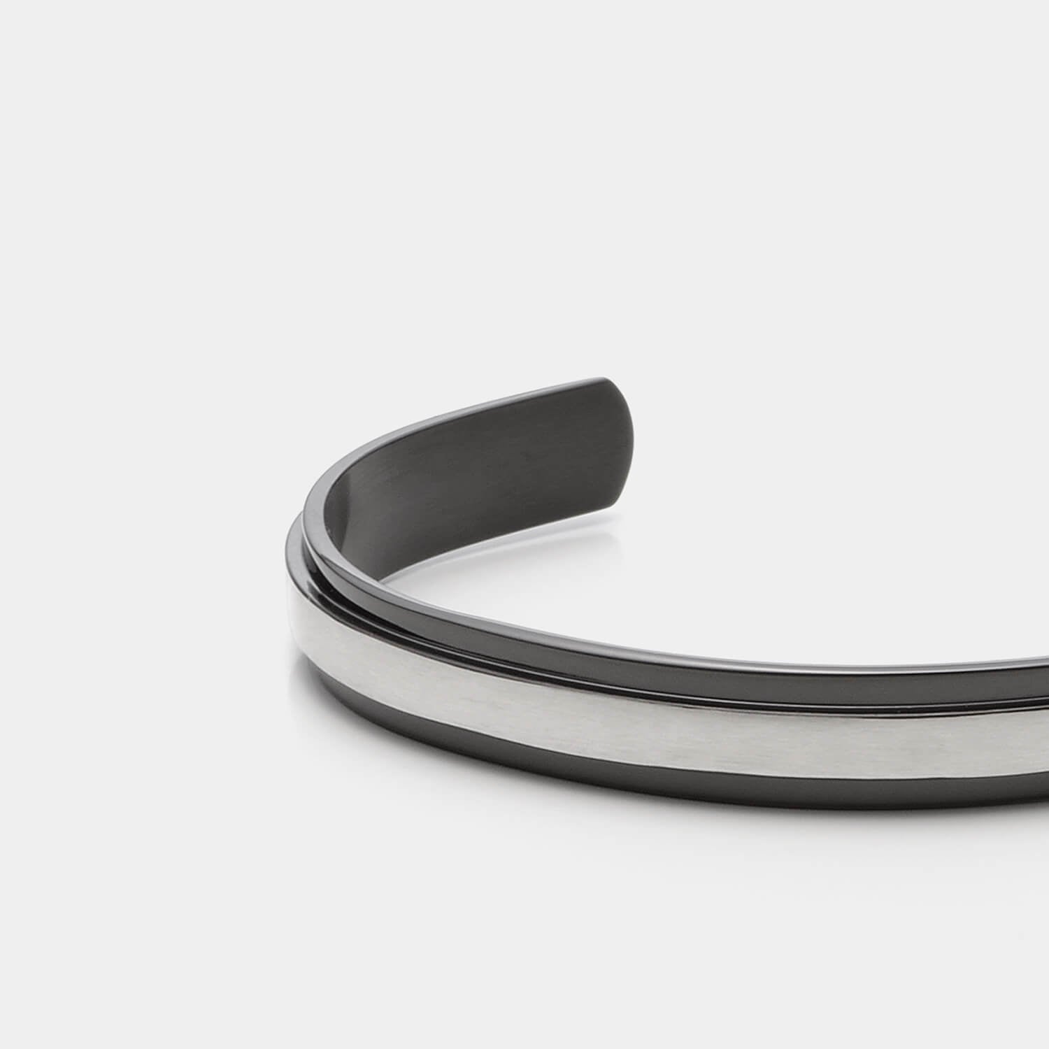 Gesamtansicht eines Armreifs aus schwarzem Edelstahl mit erhabener, silberfabener Mittelfläche.