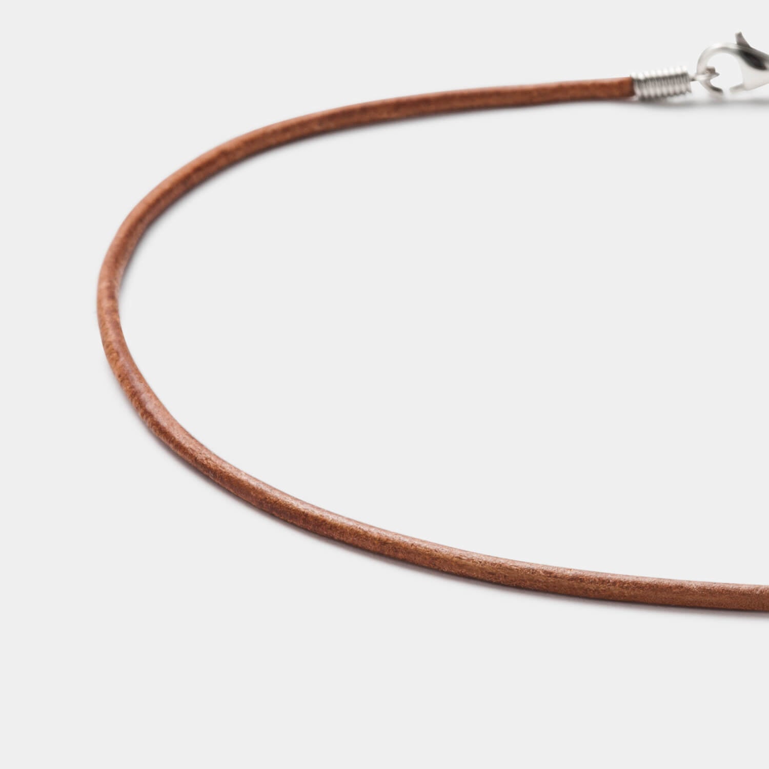 Detailansicht eines runden, braunen Lederbandes mit Karabinerverschluss aus antiallergenem Edelstahl von MONOMANIA.