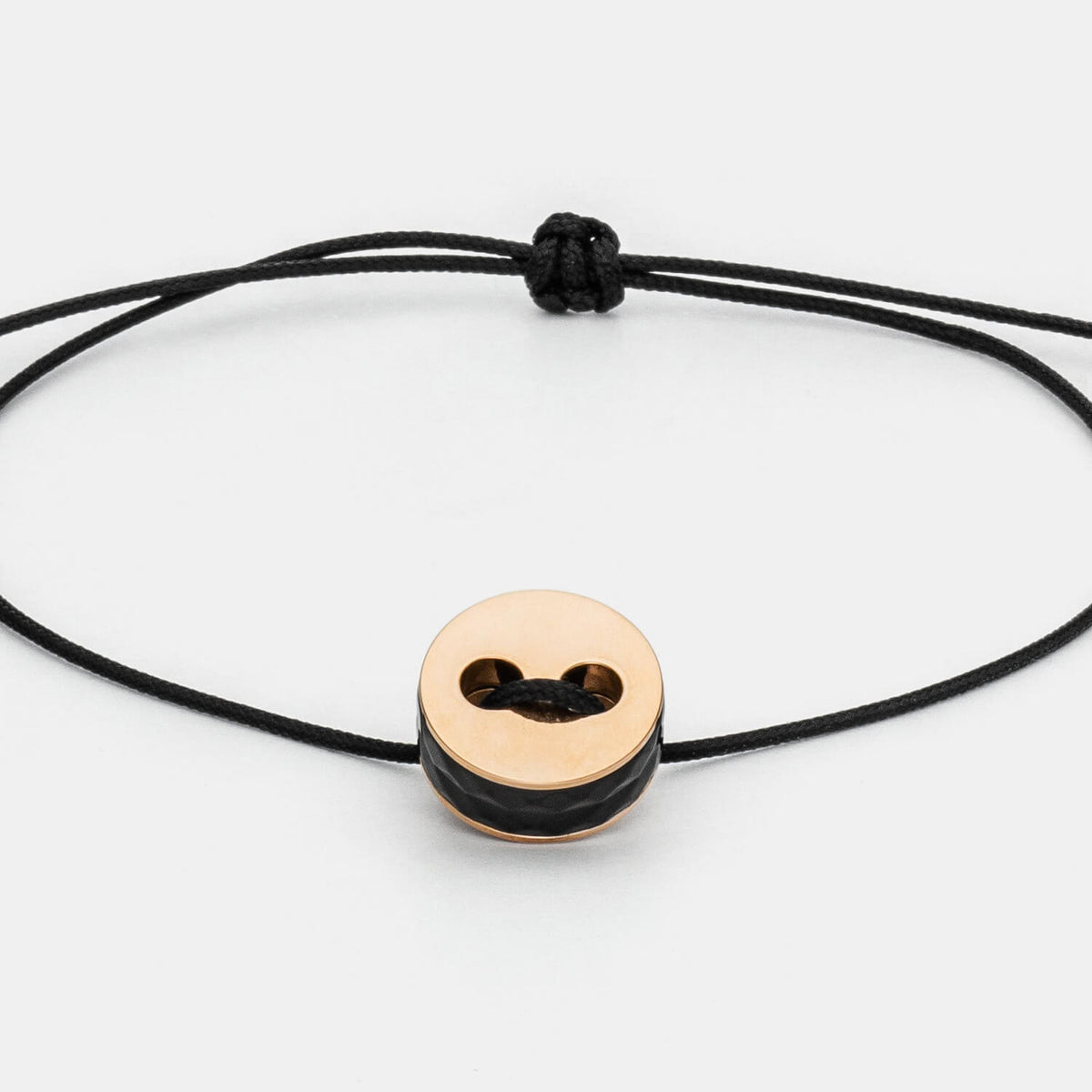 Gesamtansicht eines größenverstellbaren, schwarzen Armbandes mit roséfarbenem Anhänger aus antiallergenem Edelstahl von MONOMANIA.