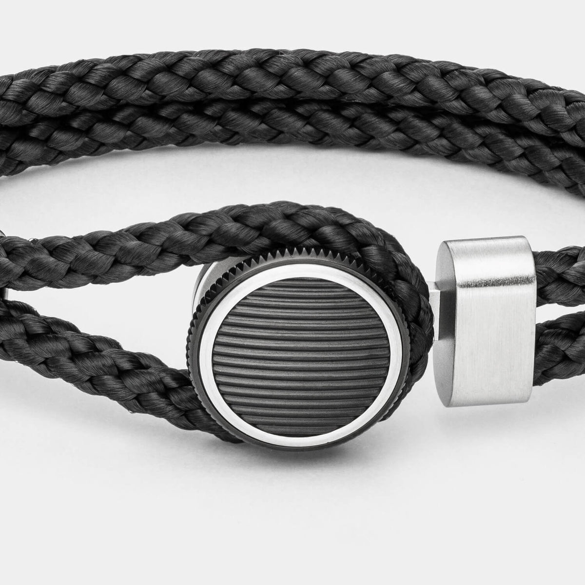 Gesamtansicht eines Armbandes mit schwarzem, geflochtenen Textil und rundem, schwarzen Verschluss von MONOMANIA.